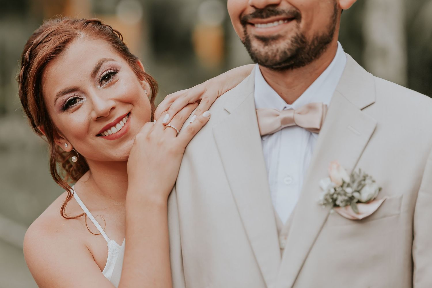 Retrato primer plano: Novia sonriente apoya cabeza en hombro novio (traje claro, boutonnière). Boda.