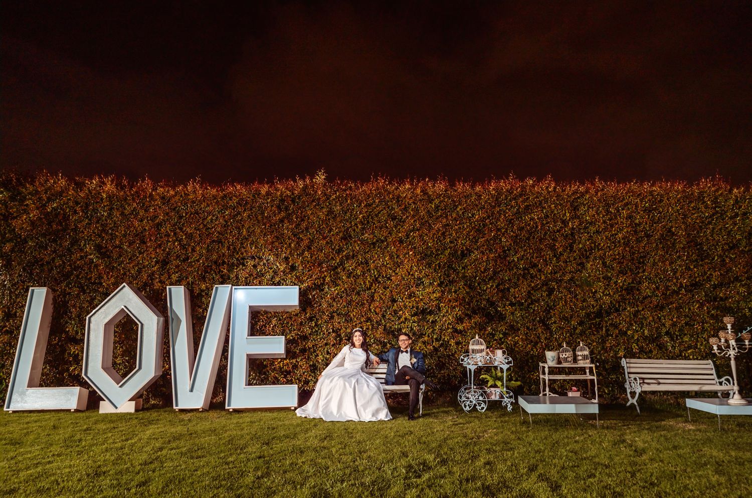 Novios sentados frente a grandes letras iluminadas de 