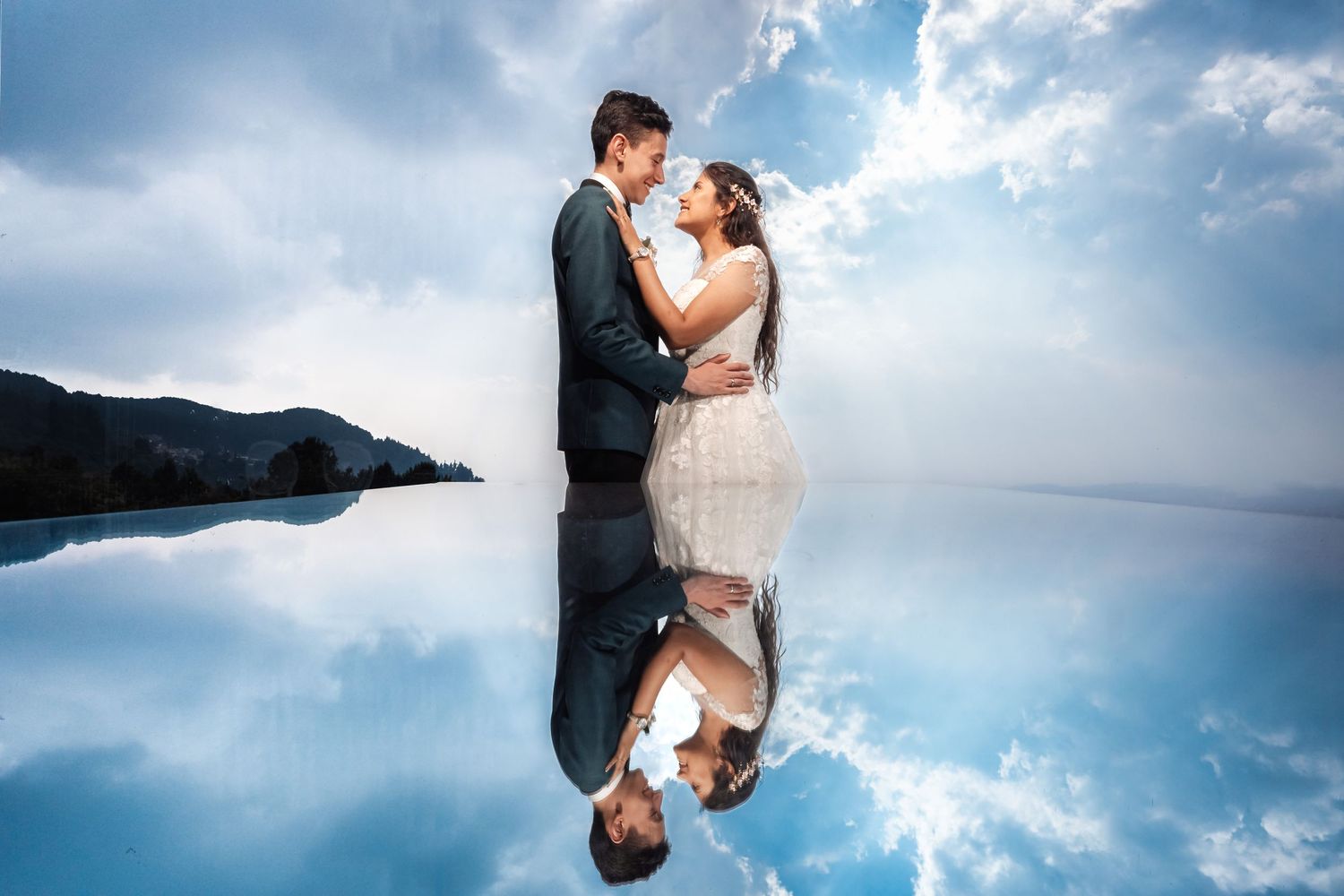 Reflejo de pareja recién casada abrazándose en reflejo de cielo nublado. Novia con vestido blanco, novio con traje oscuro. escena romántica