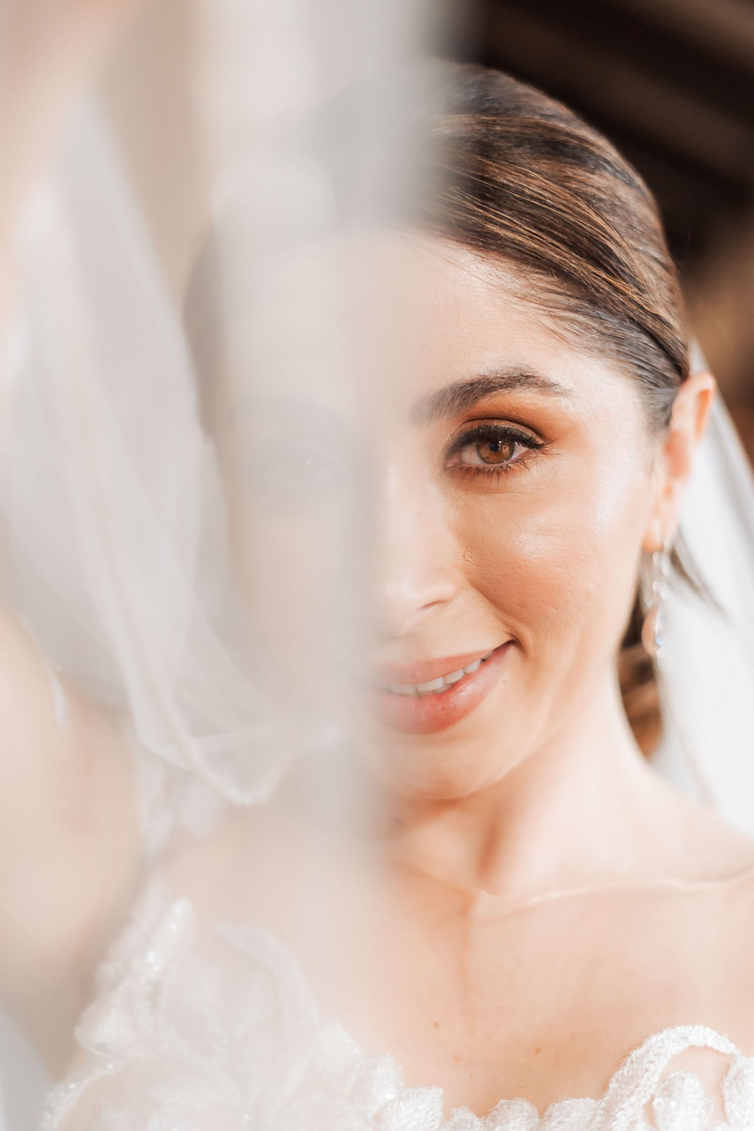 Retrato artístico primer plano: Rostro sonriente de novia visto suavemente a través de su velo etéreo. Boda.