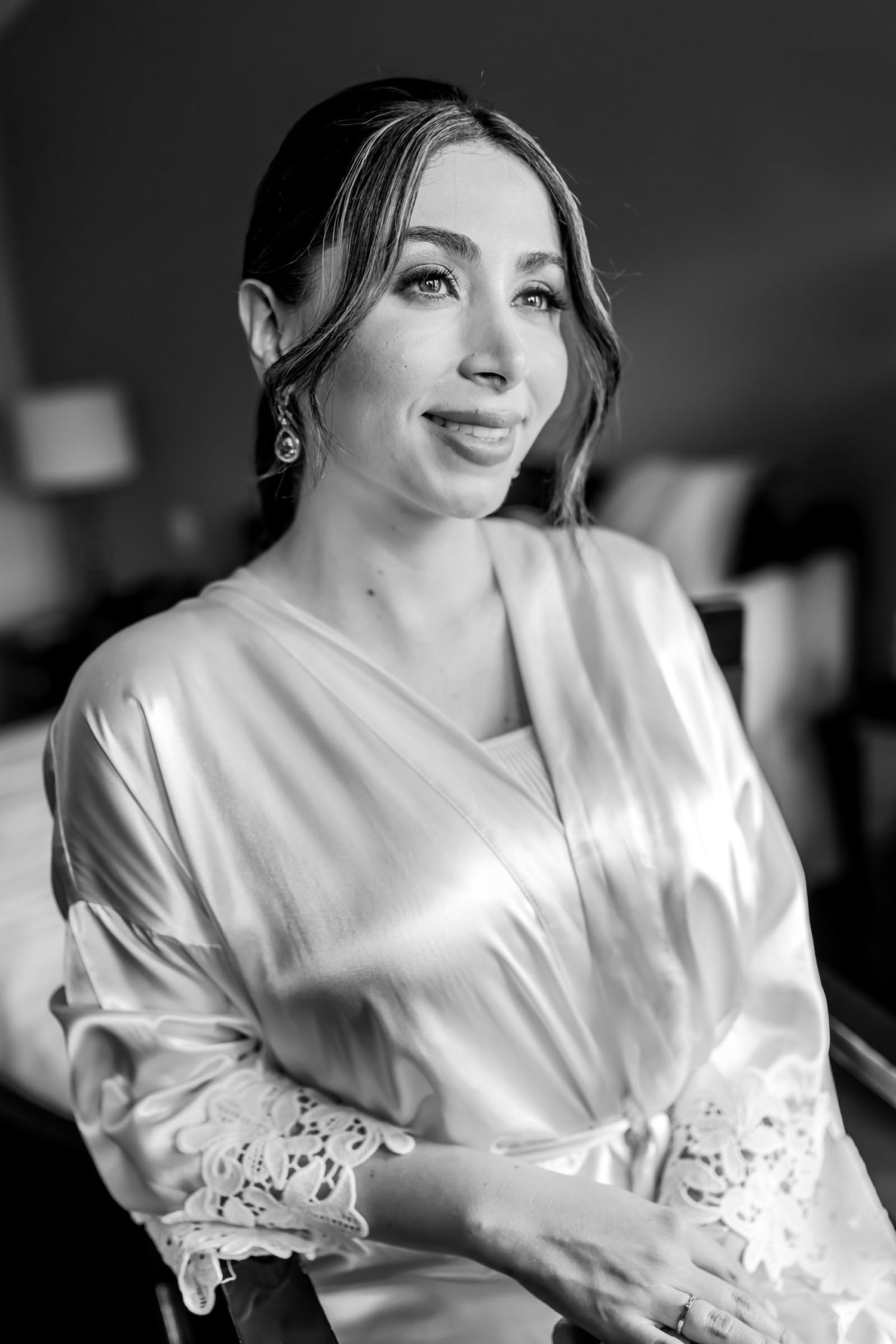 Retrato blanco y negro novia en bata mira de lado con suave sonrisa durante preparación de boda.