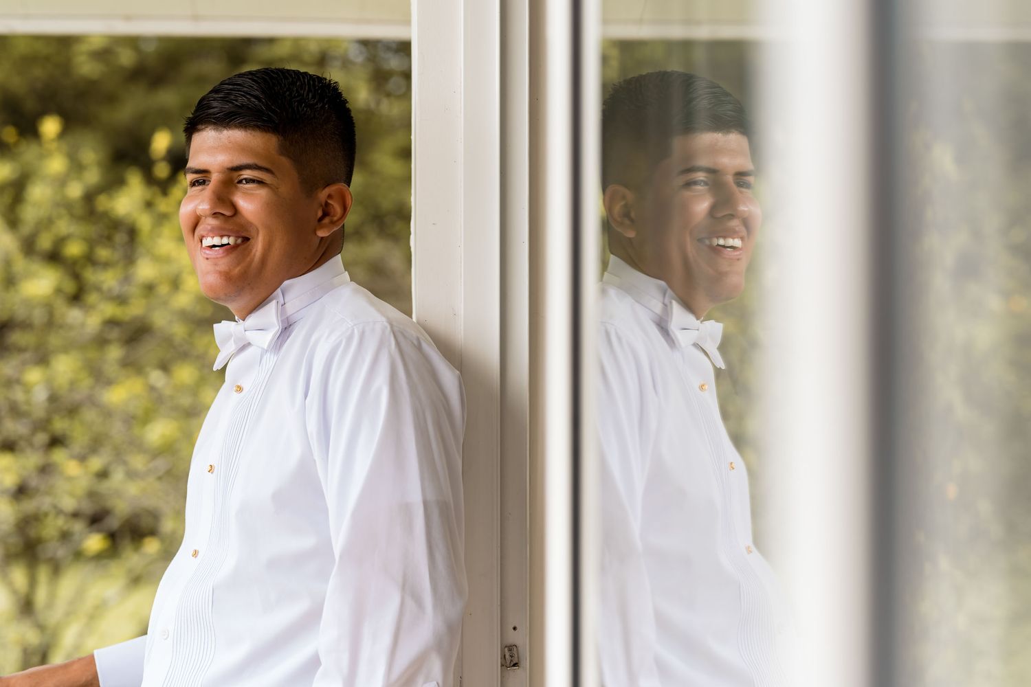 Retrato del novio mirando por la ventana, con su reflejo en el cristal, antes de la boda