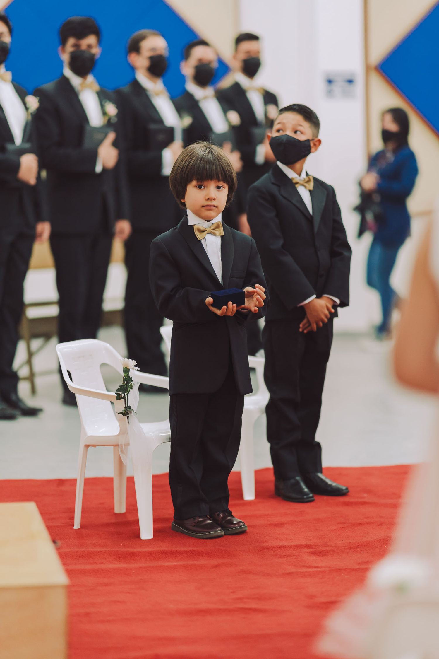 Pajecito con traje negro y mascarilla esperando en el pasillo de la boda.