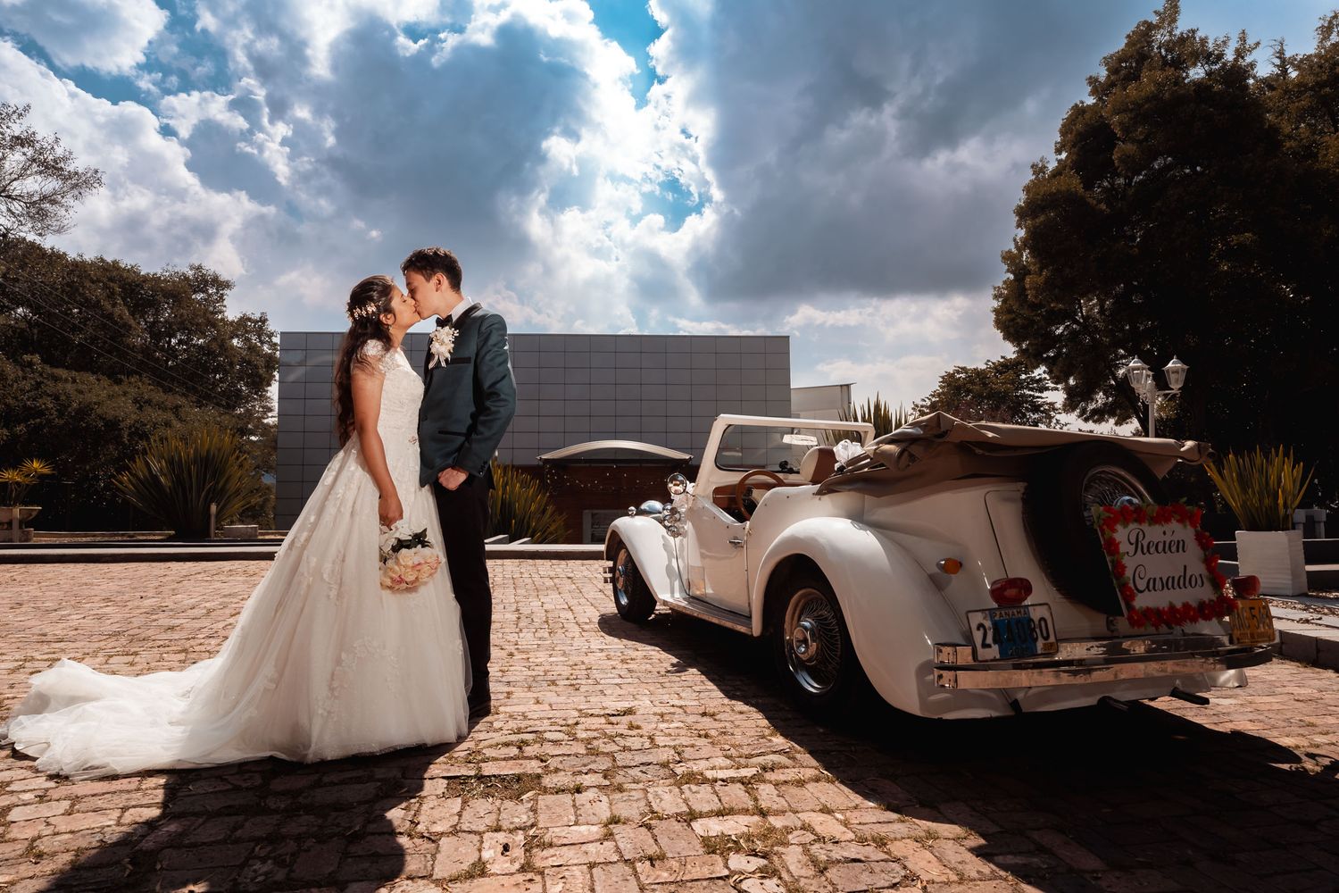 ecién casados sonrientes posando junto a coche de boda vintage blanco