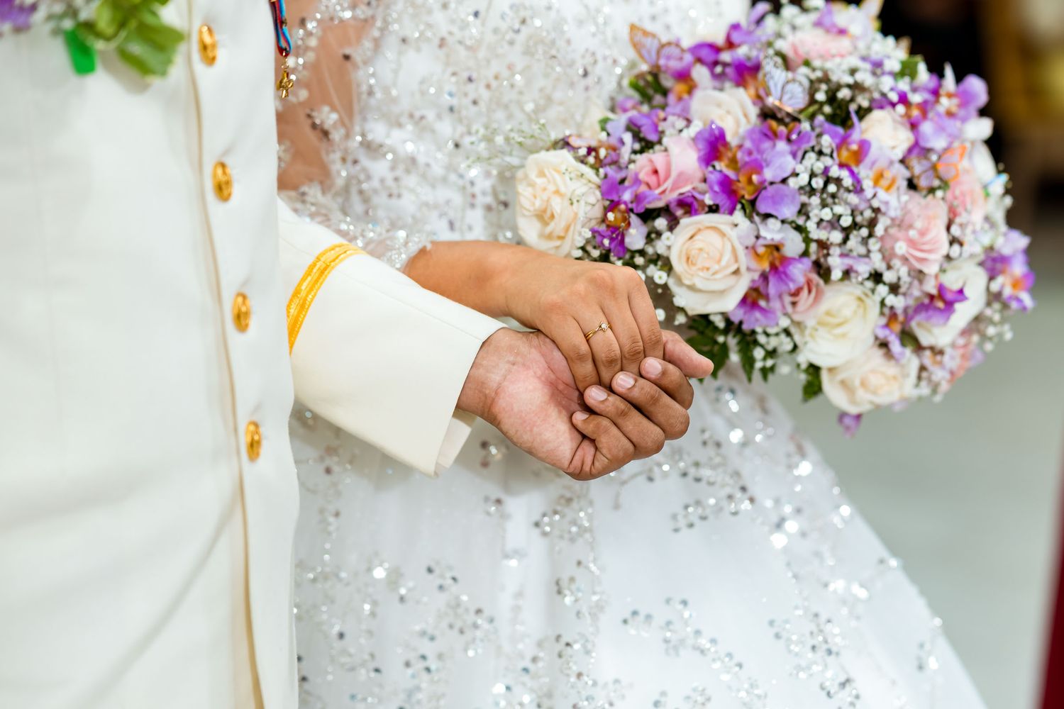 Detalle de las manos de los novios unidas sobre el ramo de la novia.