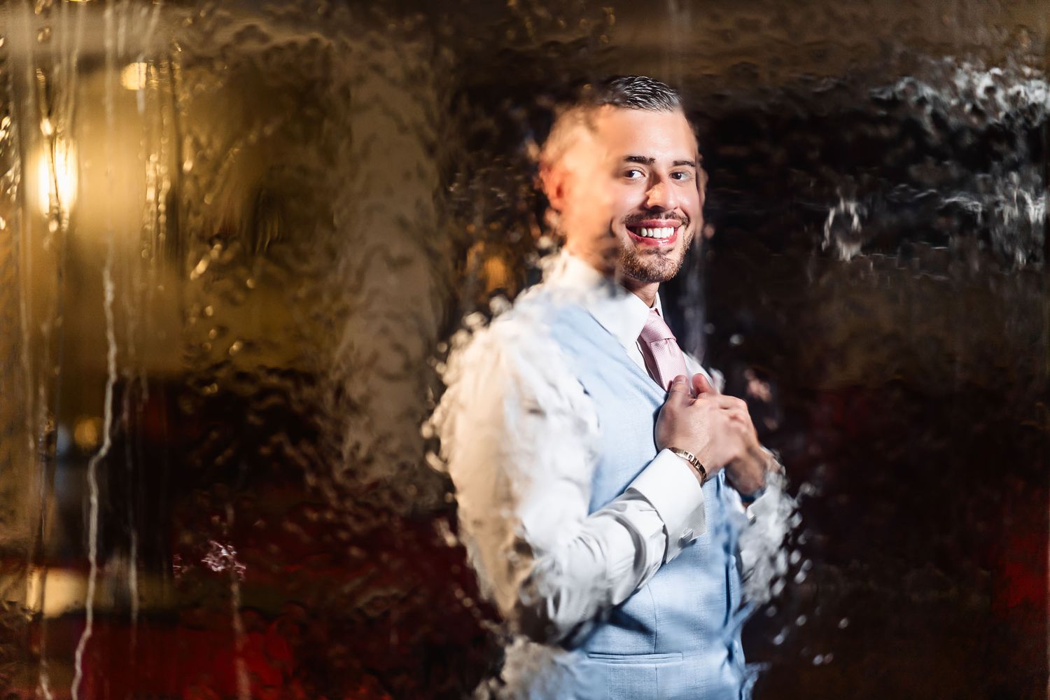 Primer plano de novio sonriendo felizmente, vistiendo chaleco azul y corbata rosa. Foto de boda.