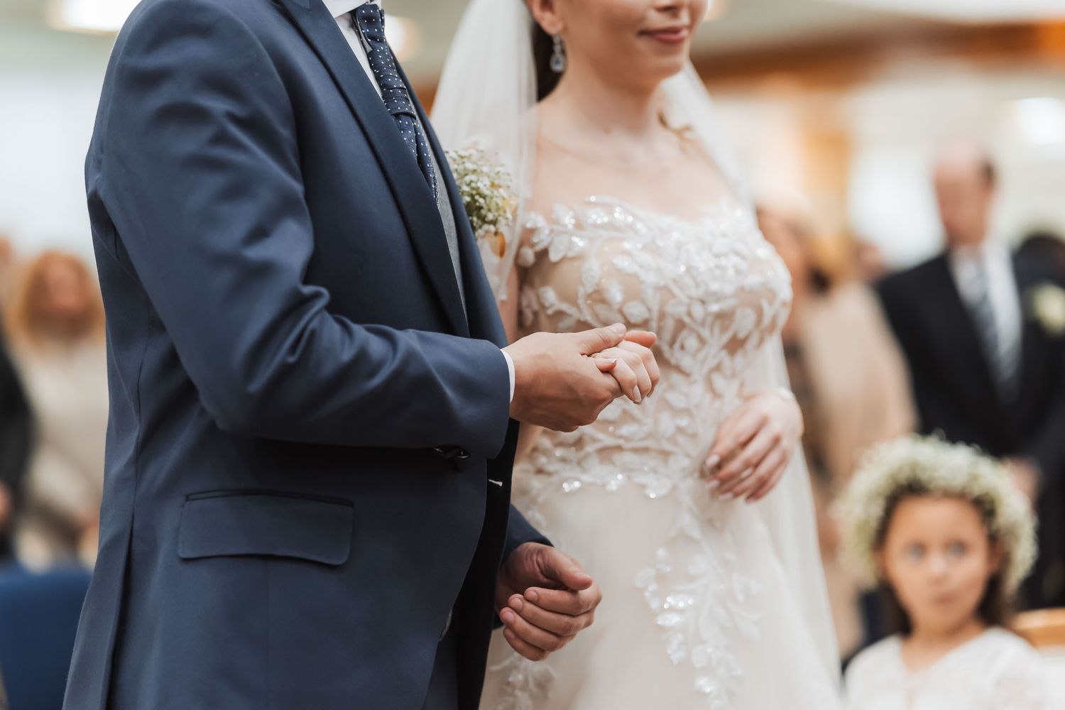 Detalle cercano: Novios tomados de la mano fuertemente durante ceremonia de boda IDMJI; vestido bordado novia.