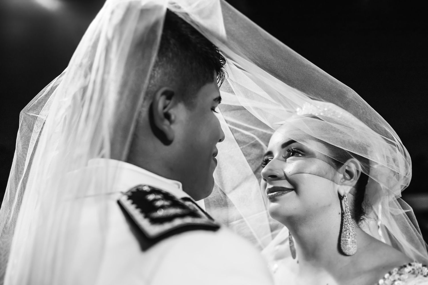 Retrato artístico en blanco y negro de los novios mirándose afectuosamente bajo el velo de la novia