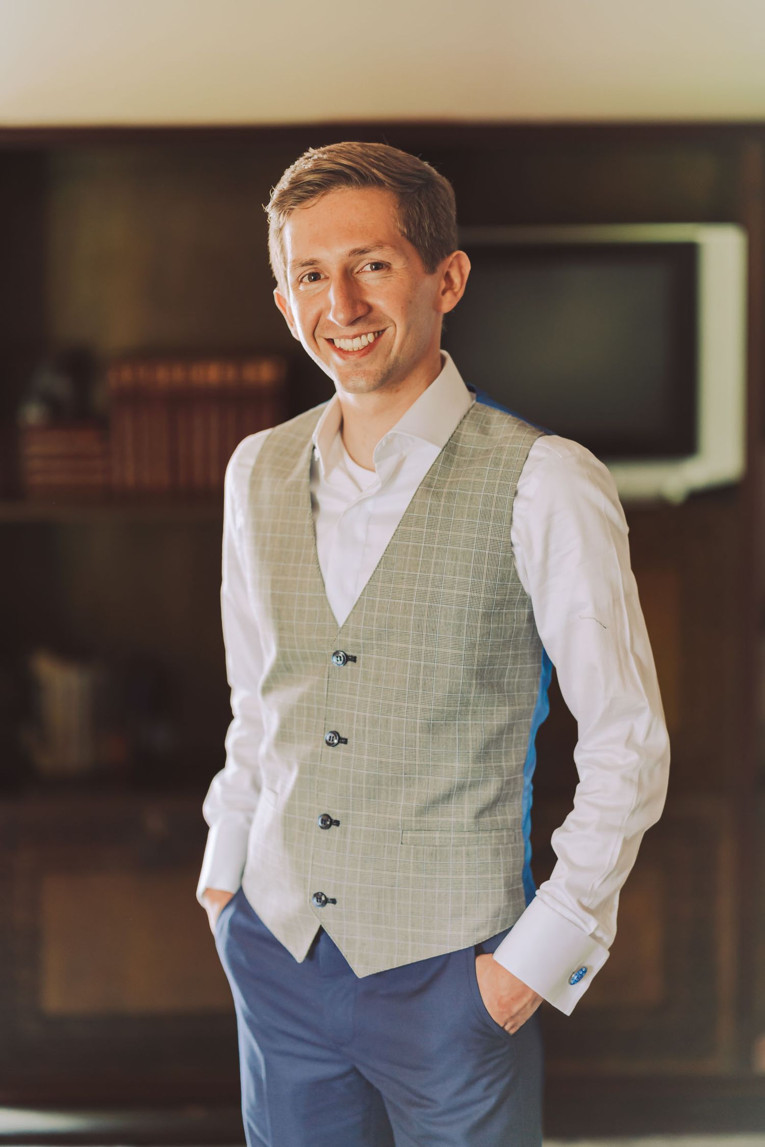 Retrato del novio sonriente con chaleco gris en su boda.