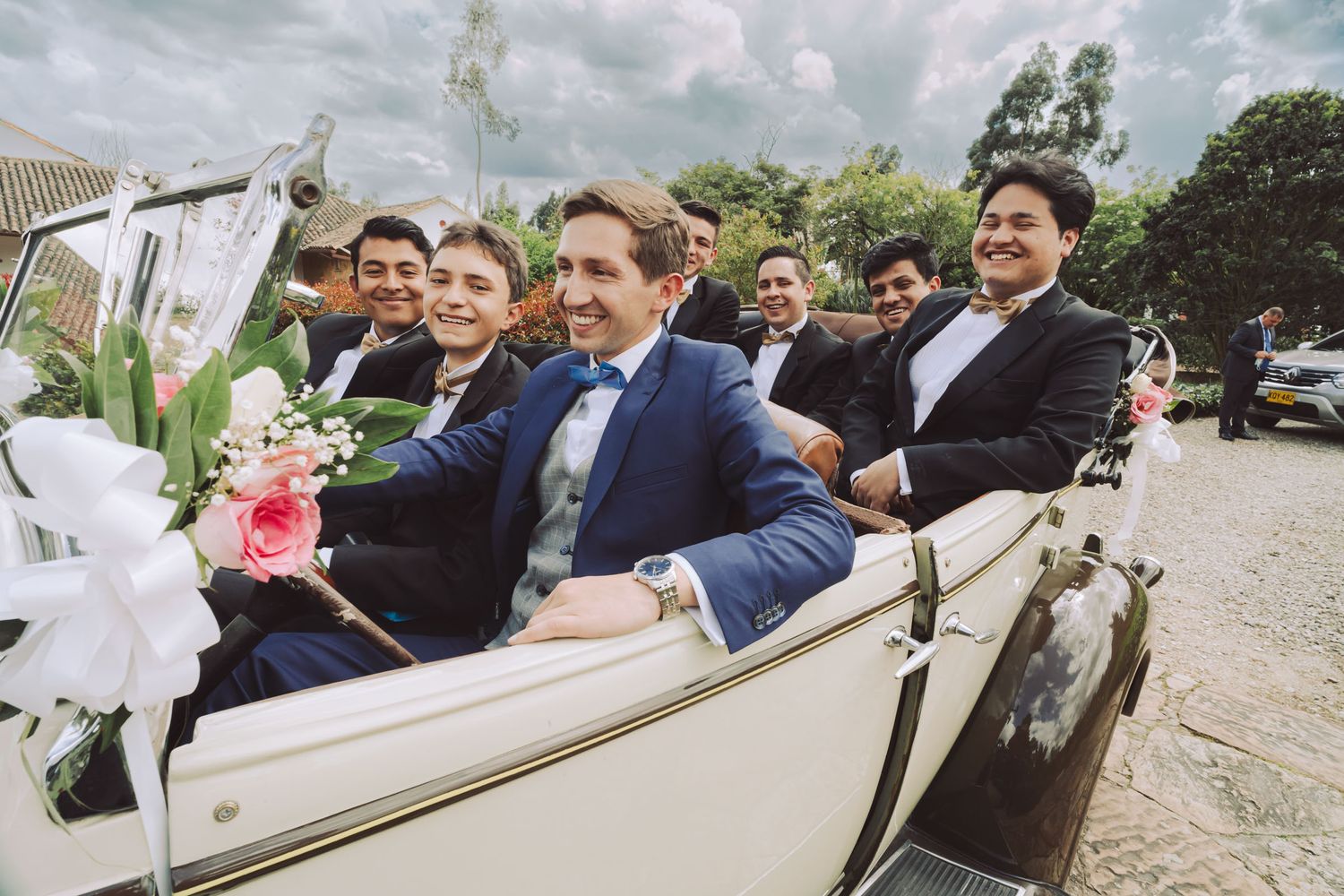 Novio y padrinos celebrando en un coche convertible antiguo.