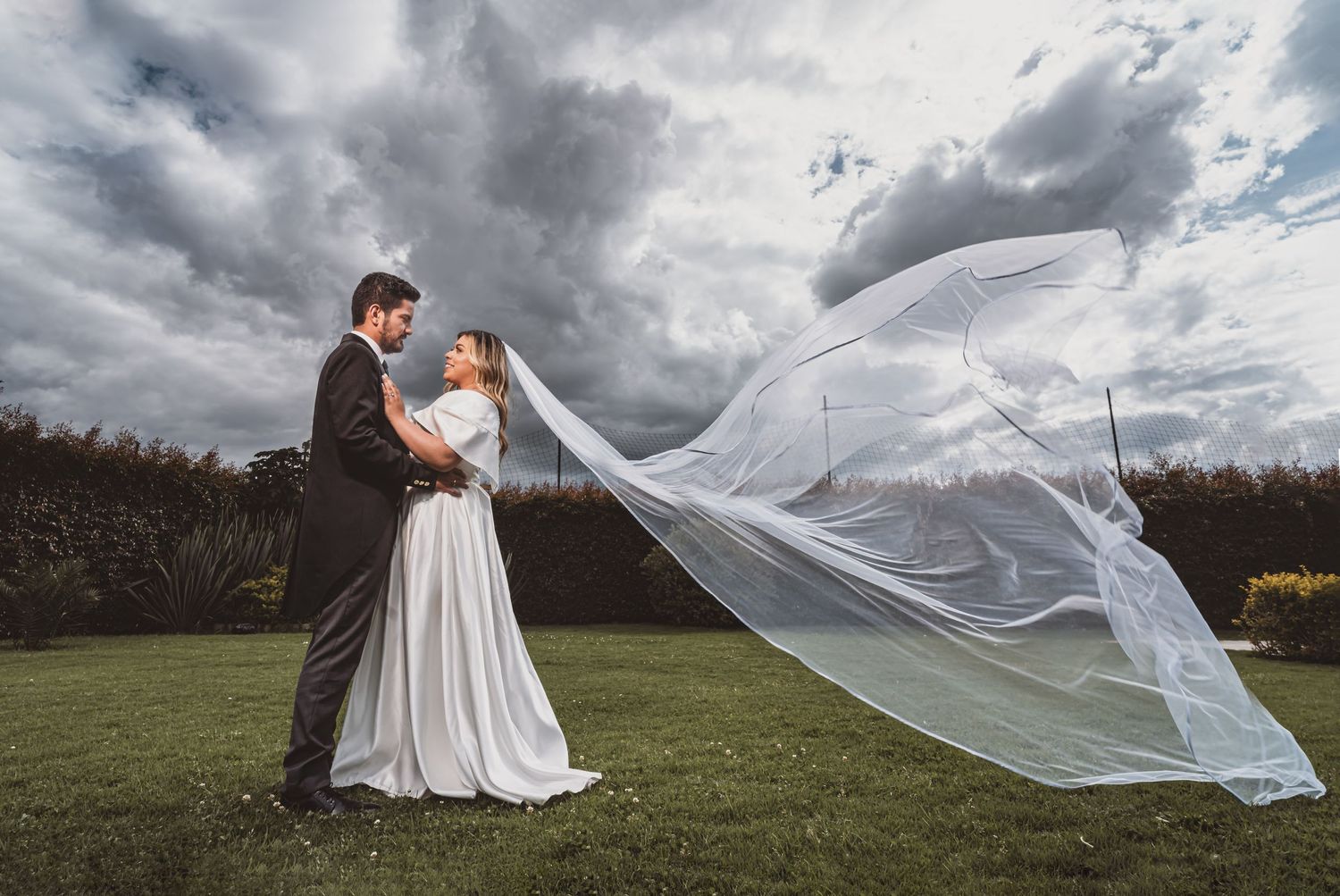 Novios se besan apasionadamente en campo al atardecer; siluetas árboles, cielo naranja. Boda.