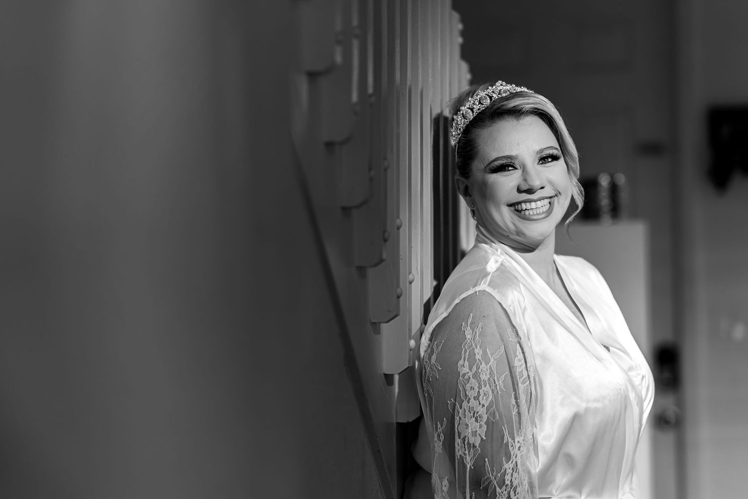 Foto B&W: Retrato novia sonriente con bata (mangas encaje) y tiara en pasillo. Preparación boda.