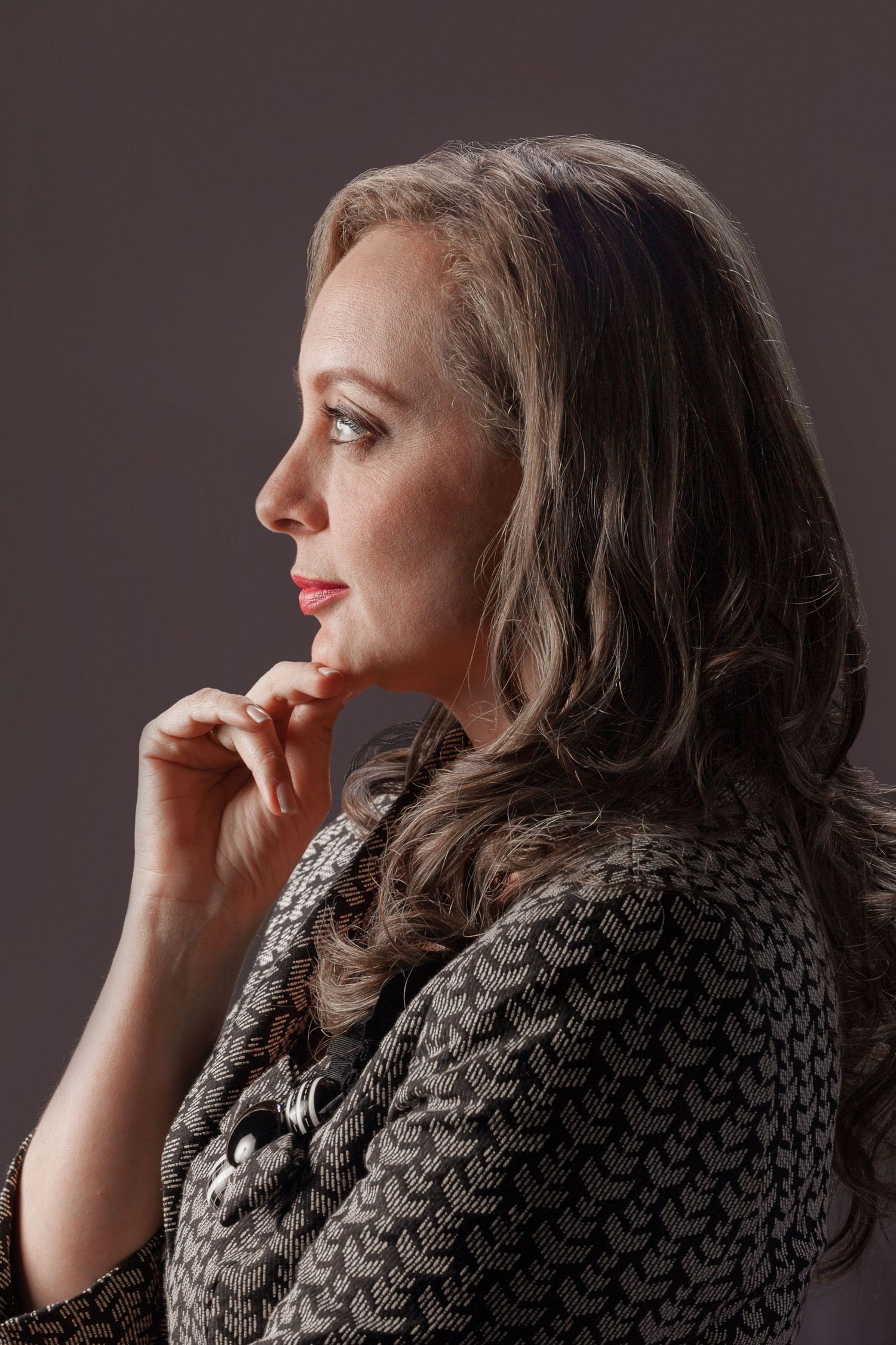 Retrato perfil mujer pensativa con blazer estampado, mano cerca barbilla; fondo gris estudio. Ana Paola Agudelo