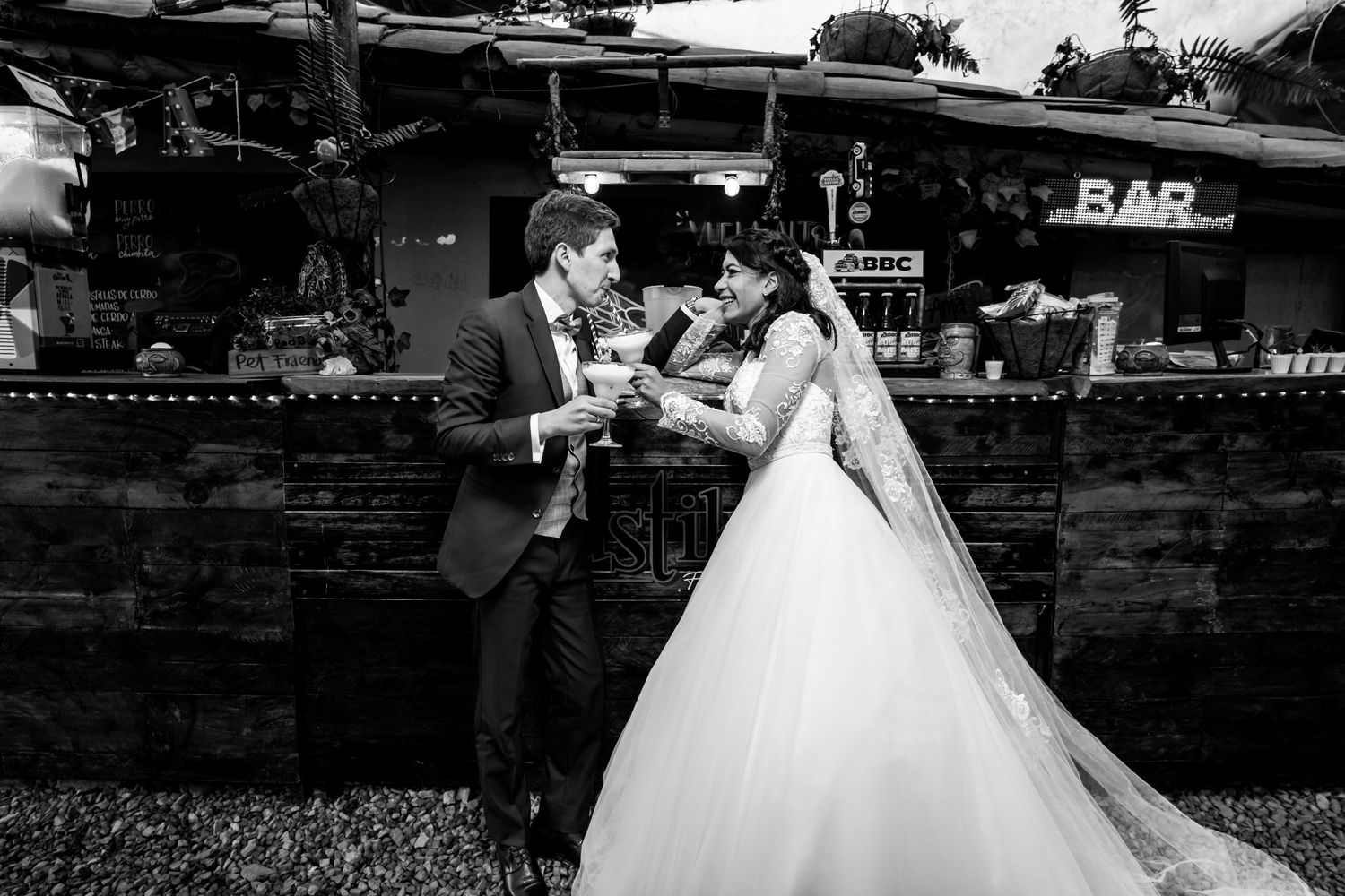 Novios brindando en una barra rústica, foto en blanco y negro de la boda.