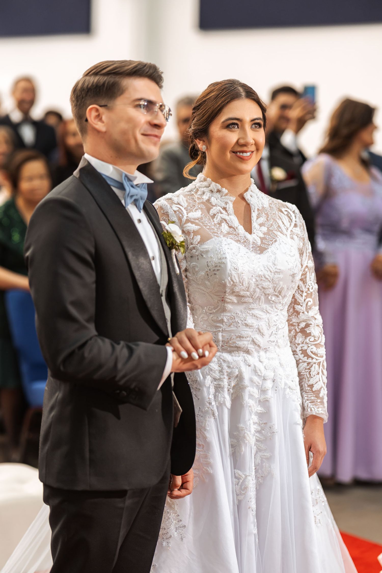 Novios sonríen juntos de pie en interior durante su boda, brazo con brazo. Momento feliz de celebración en boda IDMJI