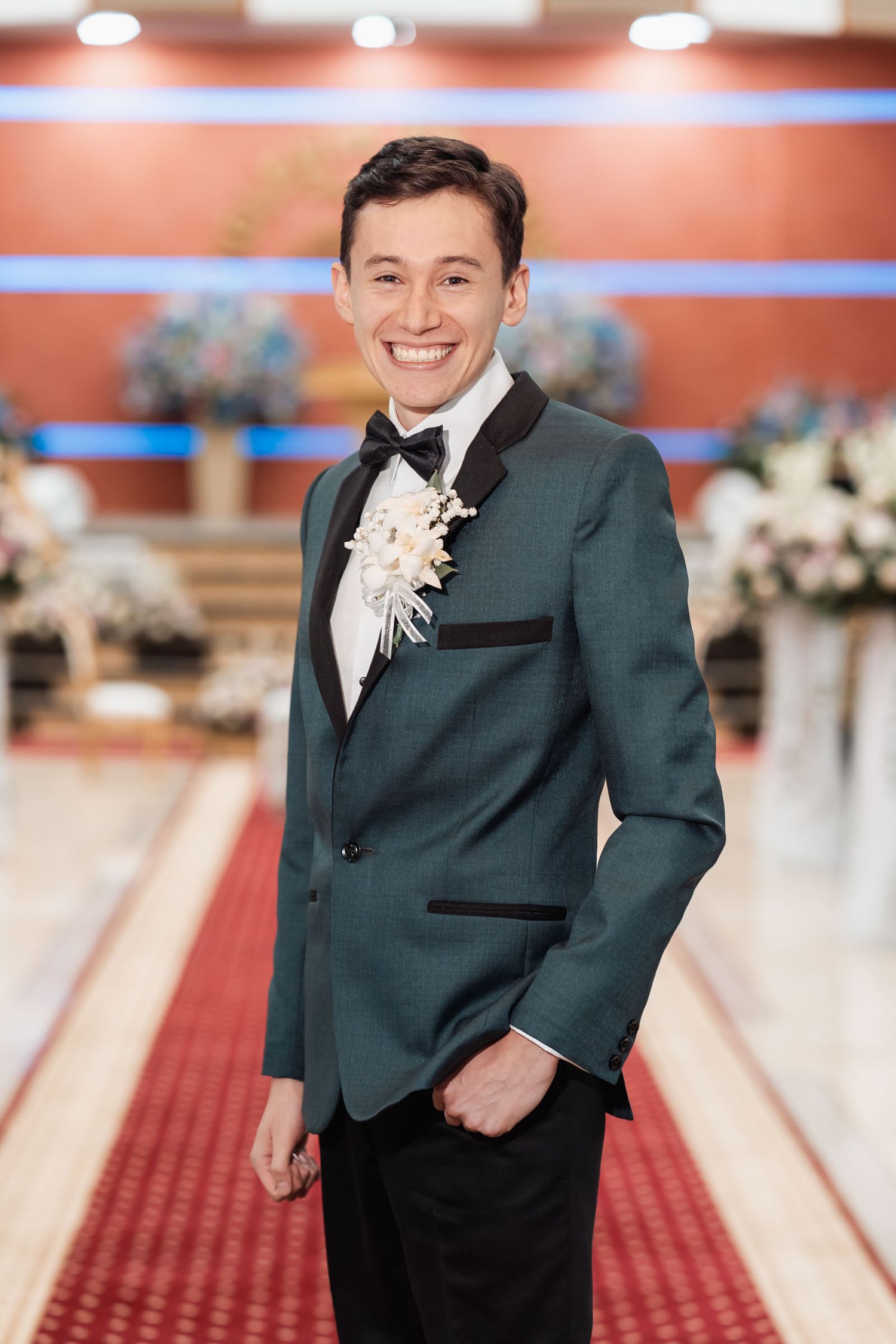 Novio elegante con traje verde azulado posando solo en alfombra roja de boda