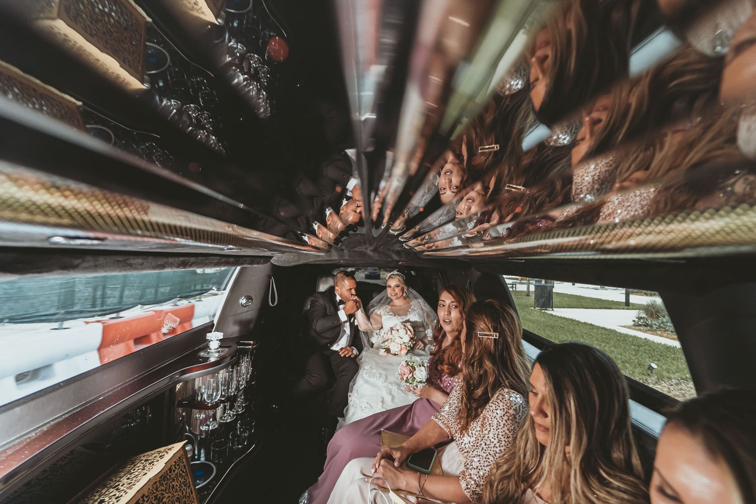 Novios y cortejo nupcial sonríen dentro de limusina; vista interior amplia con techo reflectante. Boda.