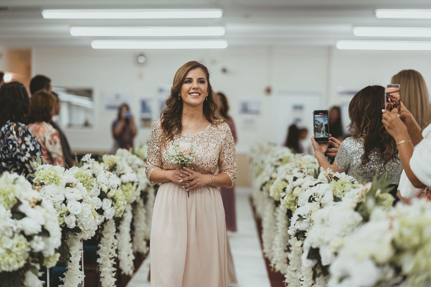 Damas de honor sonrientes caminan por pasillo iglesia en procesión boda; vestidos largos elegantes.