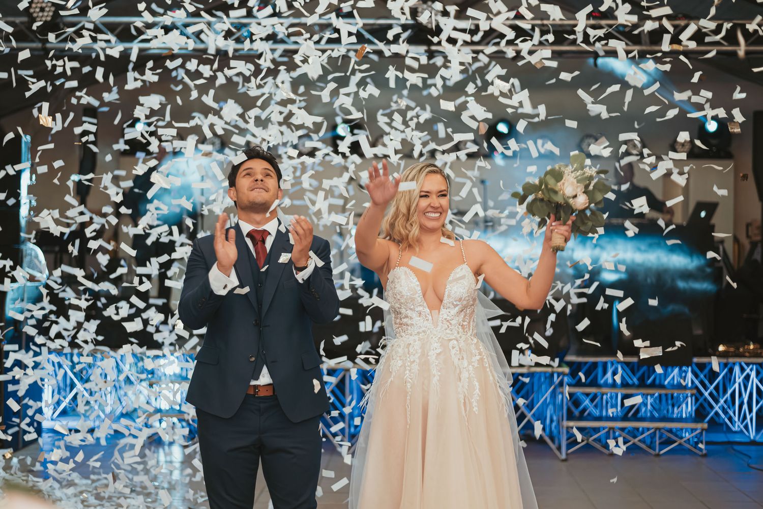 Recién casados festejando bajo una explosión de pétalos blancos. Sonrisas y alegría en su celebración de boda.