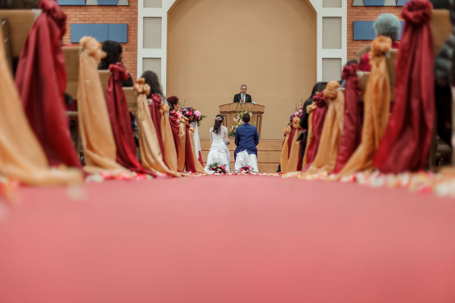 Novios sentados frente al altar durante ceremonia en iglesia en una boda IDMJI, rodeados de decoración y público.
