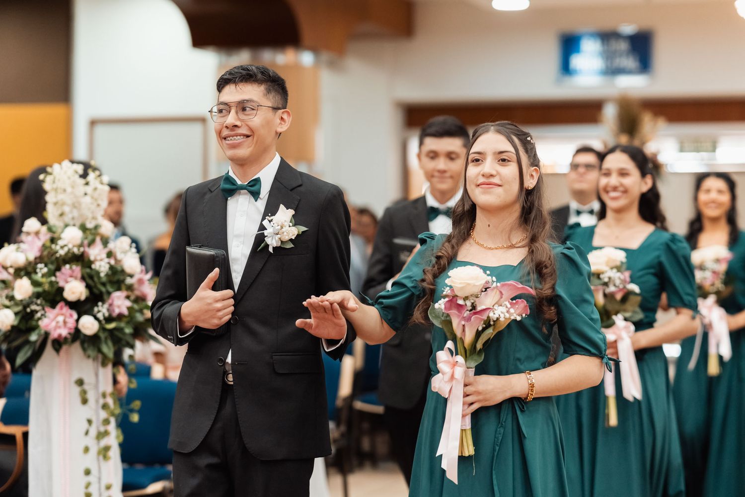Novio y madrina caminando por pasillo de iglesia seguidos por cortejo de damas de honor