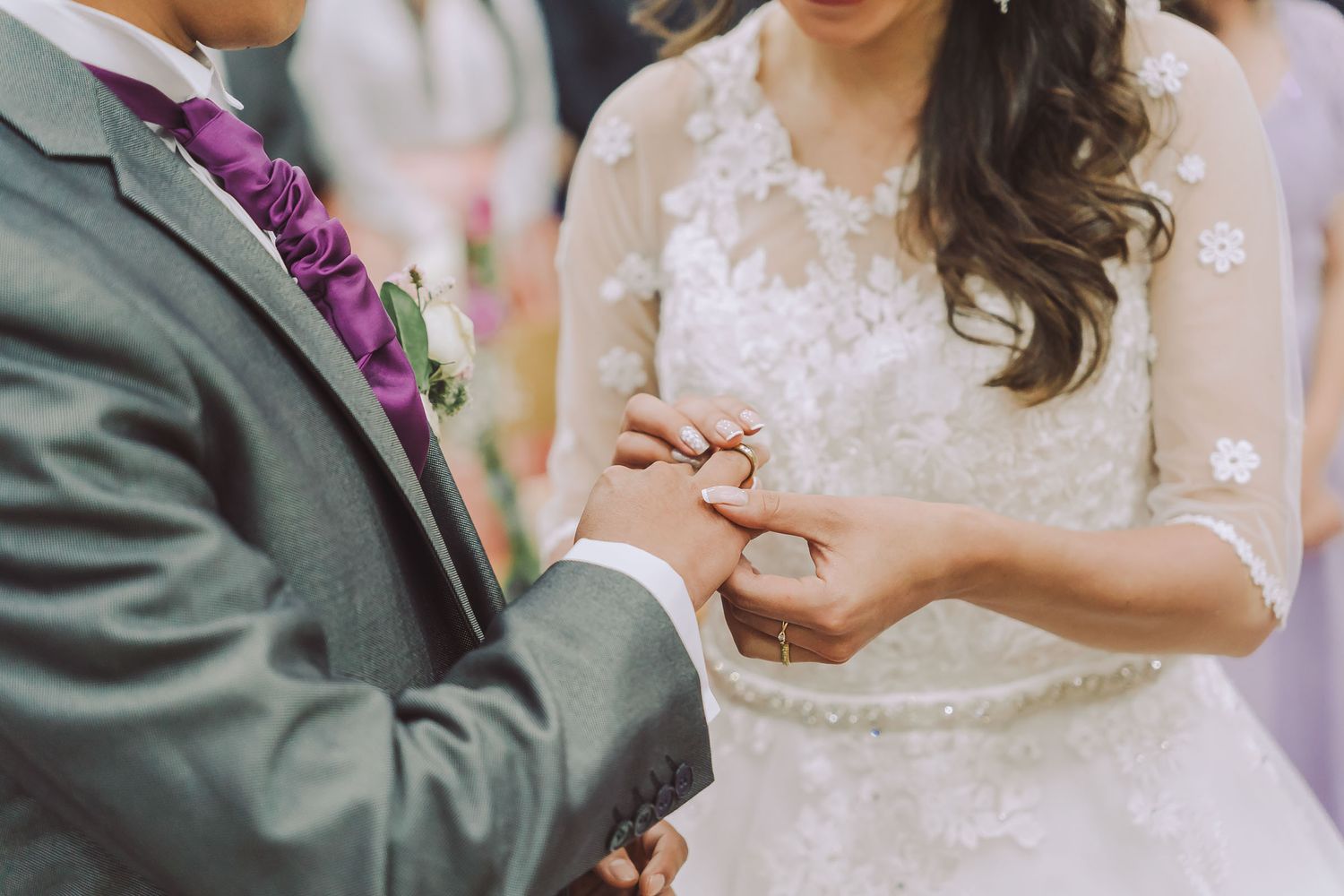 Detalle cercano: Novia coloca anillo de boda en dedo del novio durante ceremonia; vestido encaje.