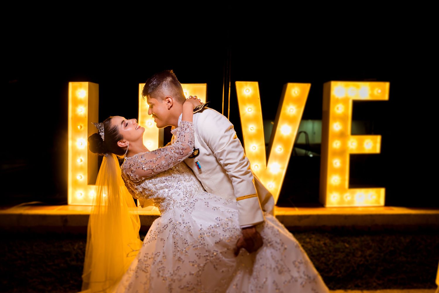 Novios se besan frente a un letrero 'LOVE' iluminado en su boda en Villavicencio.
