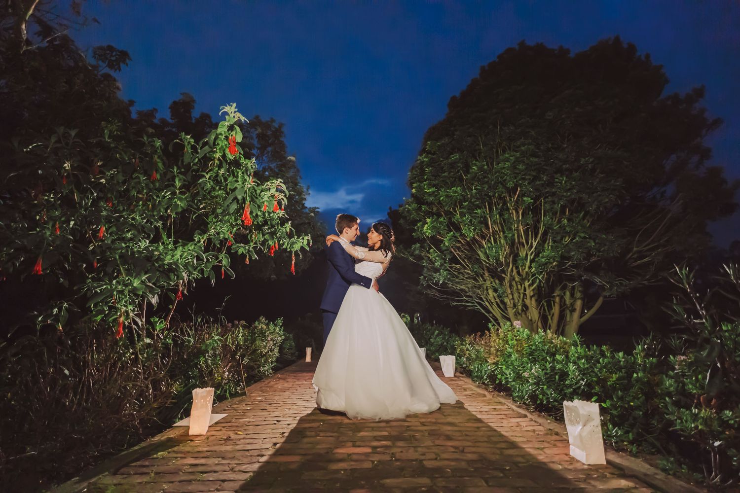 Novios abrazados de noche en un sendero de jardín iluminado en Cajicá