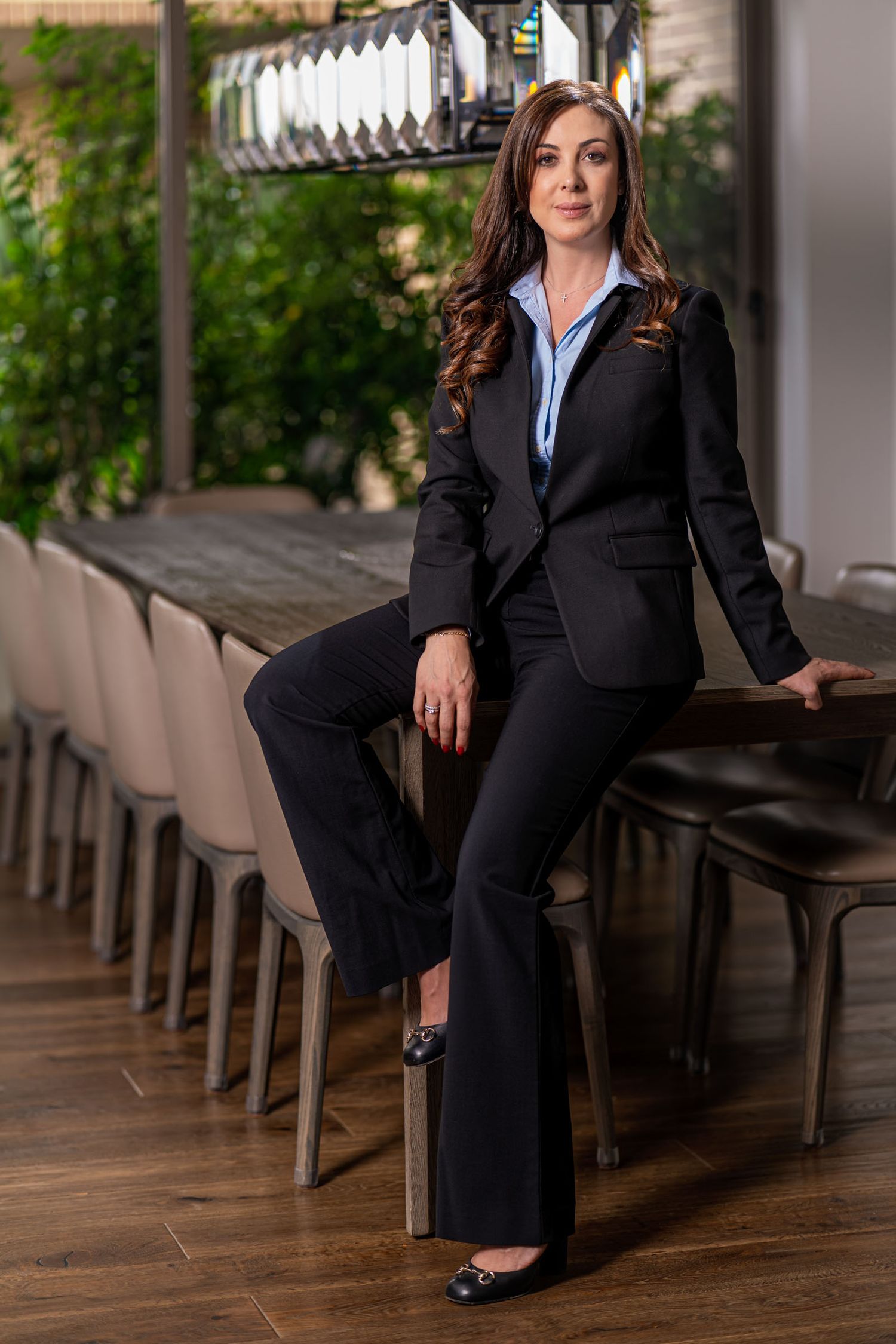 Mujer profesional con traje negro posa sentada en mesa de conferencias moderna; entorno oficina elegante. Sandra Vélez