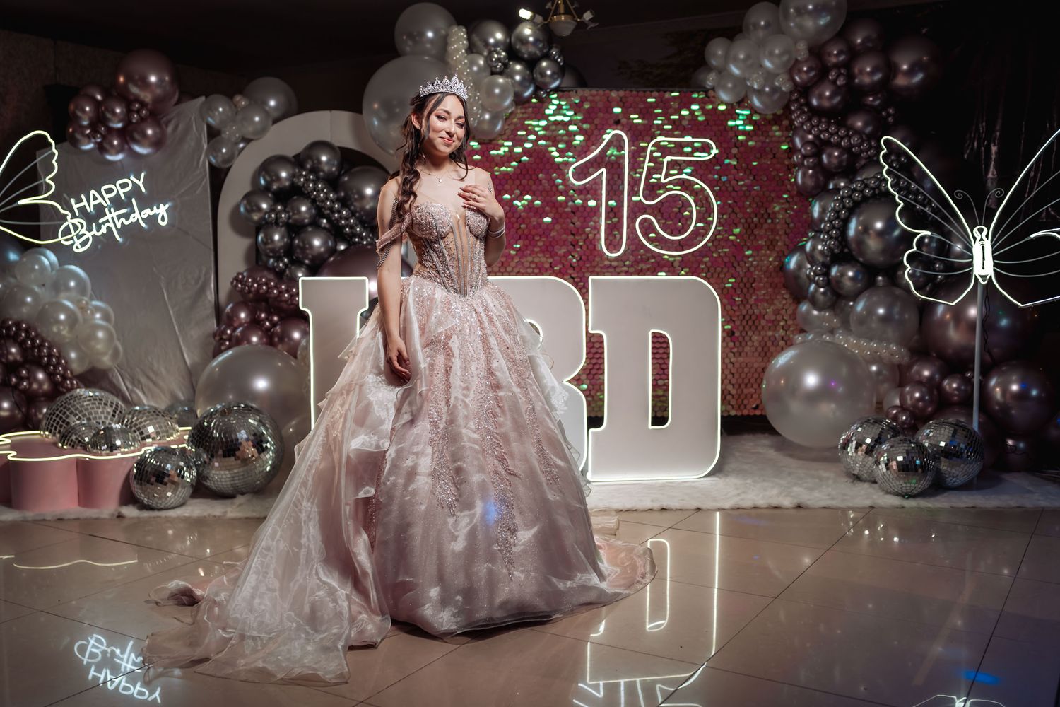 Joven quinceañera posa con vestido princesa rosa brillante y tiara; fiesta 15 decorada, globos, neón, letras BRD.