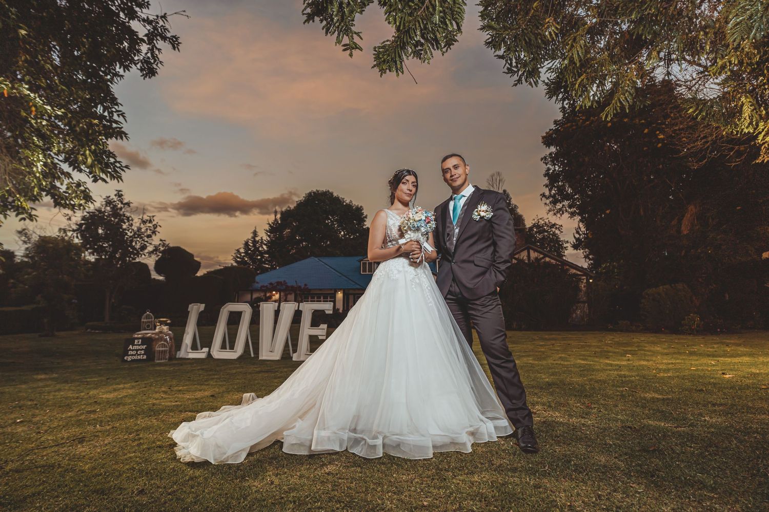 Novios posan en jardín frente a letras gigantes 