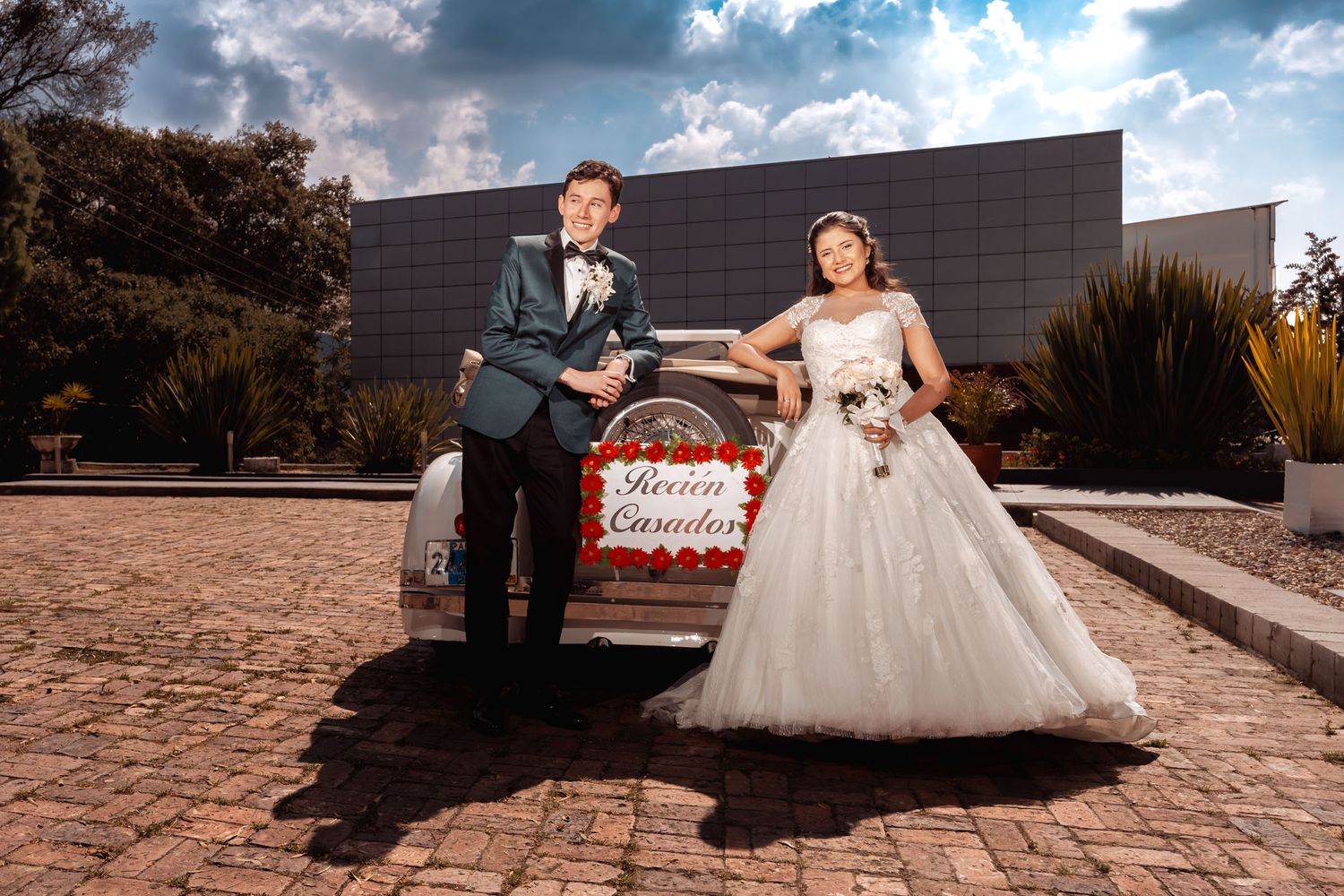 Recién casados felices posando con auto de boda blanco vintage