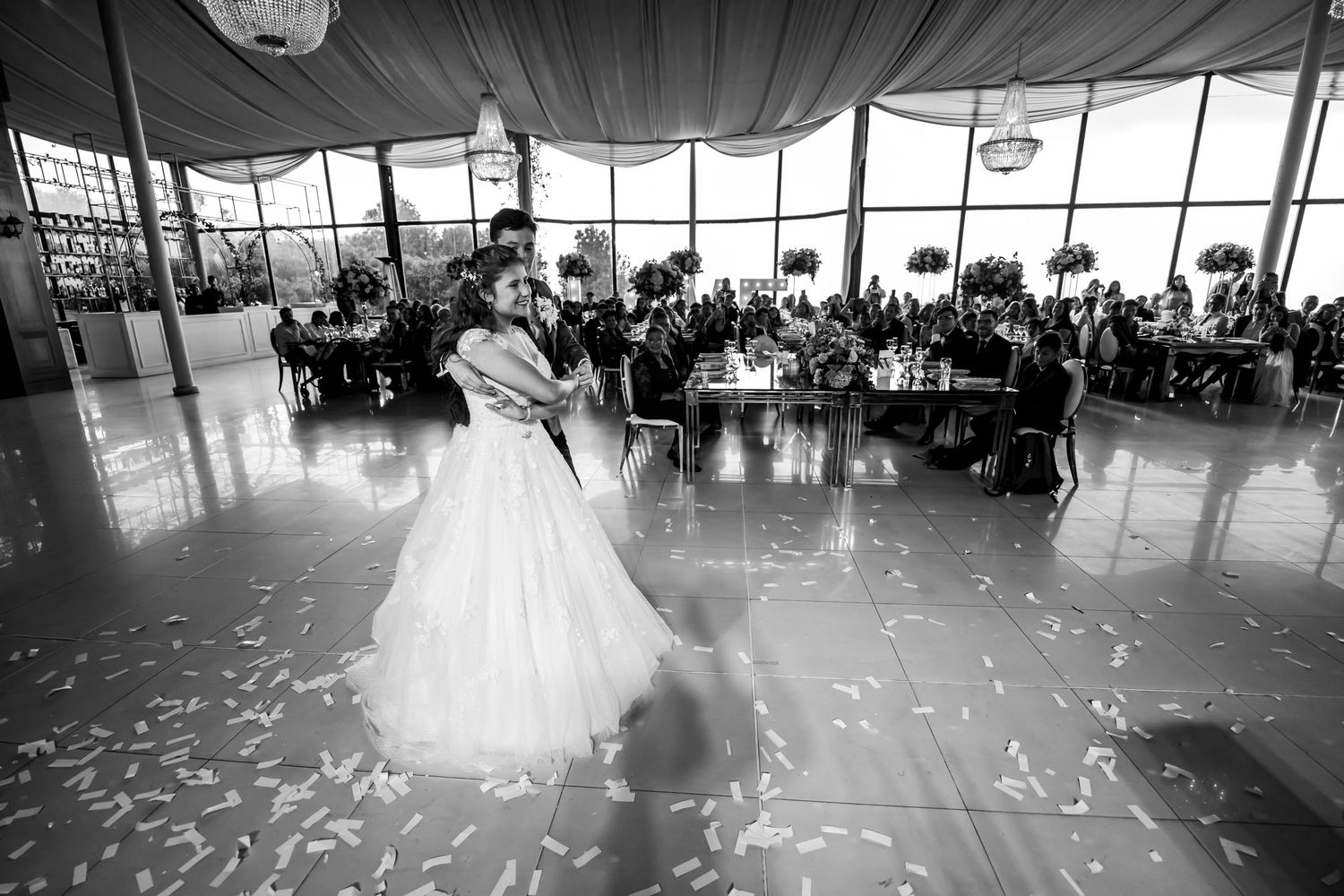 Novios bailando con energía en pista con confeti, fotografía blanco y negro.