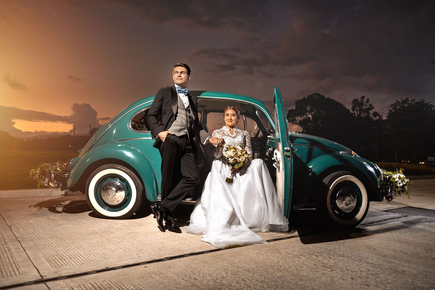 Novia sentada dentro de coche clásico verde, novio posa apoyado en la puerta exterior de noche. Foto de boda.