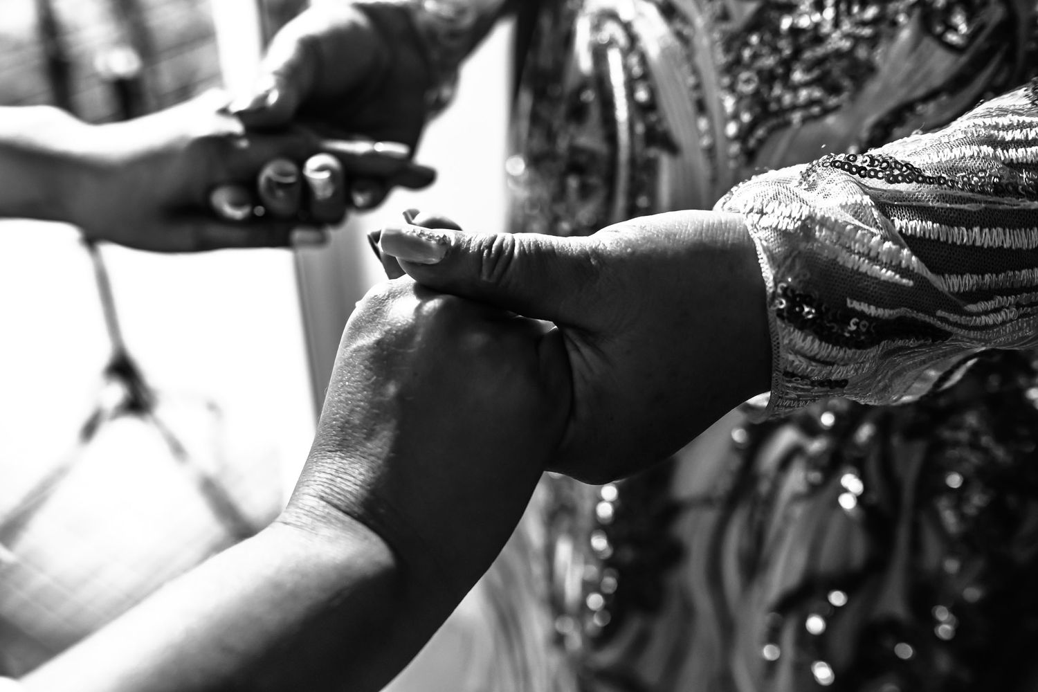 Detalle en blanco y negro de las manos de la madrina ayudando a la novia a vestirse