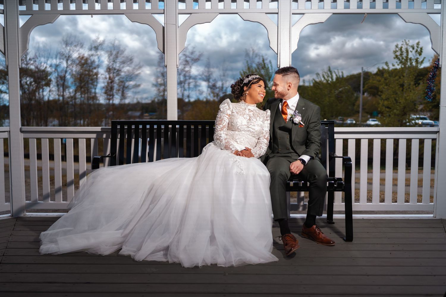 Pareja de esposos mirándose y riendo, sentados con su traje de novios en una cabaña típica de Estados Unidos. Paisaje natural de fondo
