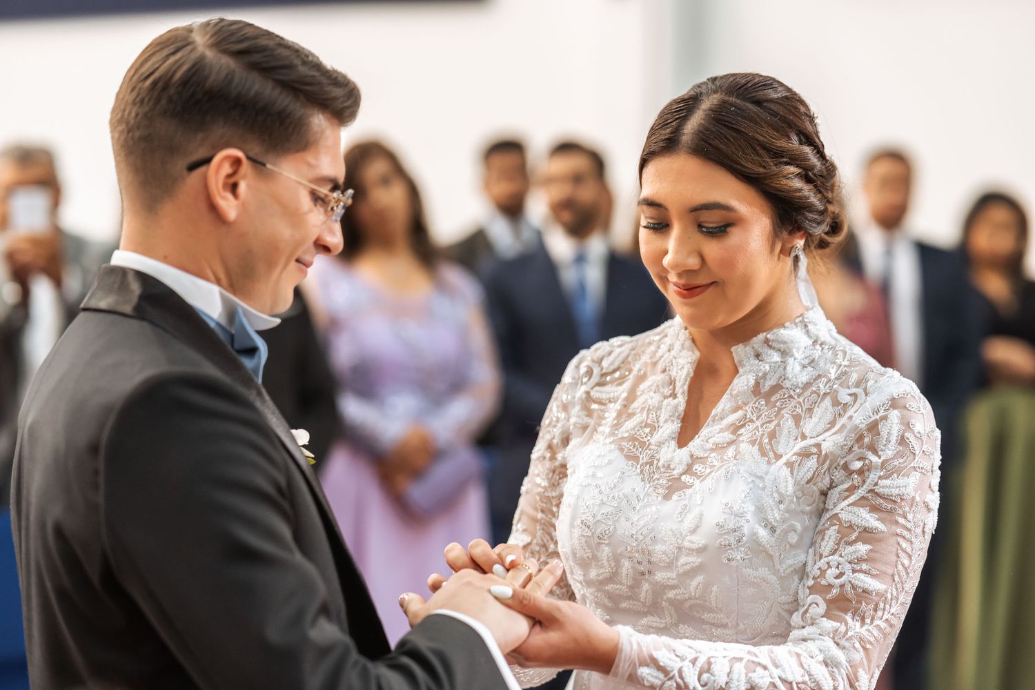 Novios se toman de las manos y se miran emotivamente durante su ceremonia en boda IDMJI, con invitados detrás.