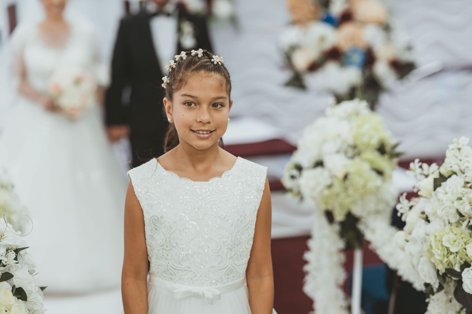 Niña de las flores (paje) sonriente con vestido blanco camina por pasillo de iglesia decorado. Ceremonia boda.