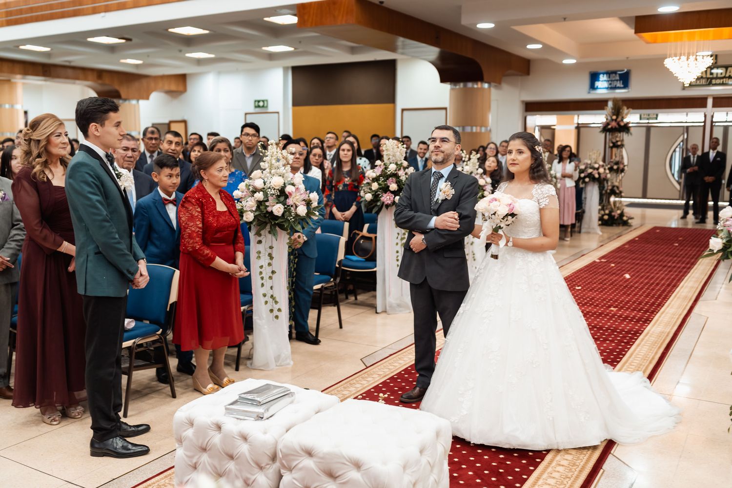 Padre entrega a novia frente al novio en iglesia con pasillo rojo