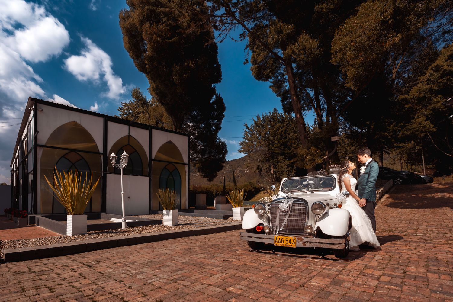 Novios con coche clásico blanco en patio colonial para boda