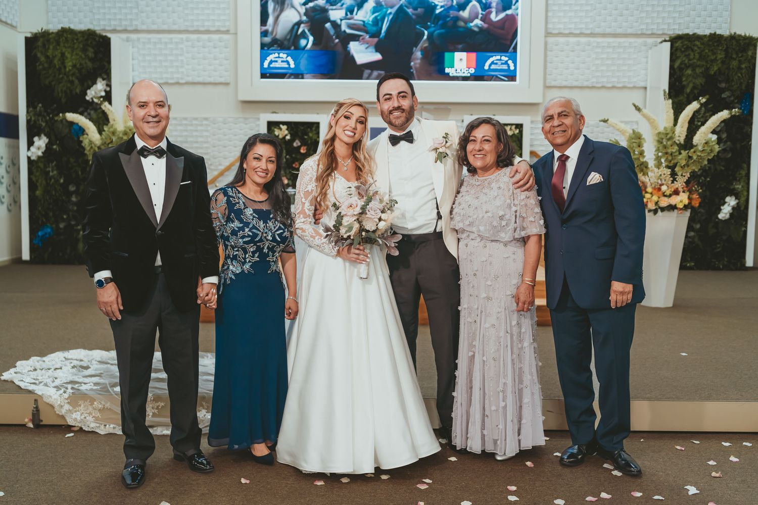 Novios posan sonrientes con sus padres o familiares cercanos en altar de iglesia. Foto familiar boda.