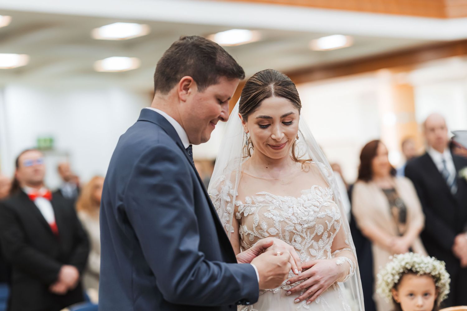 Momento íntimo boda IDMJI: Novio coloca anillo en dedo de novia sonriente durante ceremonia frente a invitados. Ceremonia