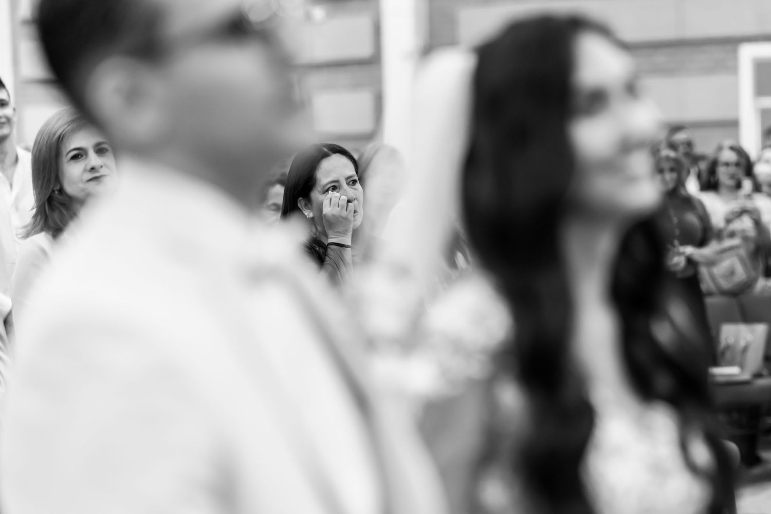 Madre reacciona emocionada, llevando mano a su rostro, durante ceremonia de boda IDMJI. Foto de boda blanco y negro.