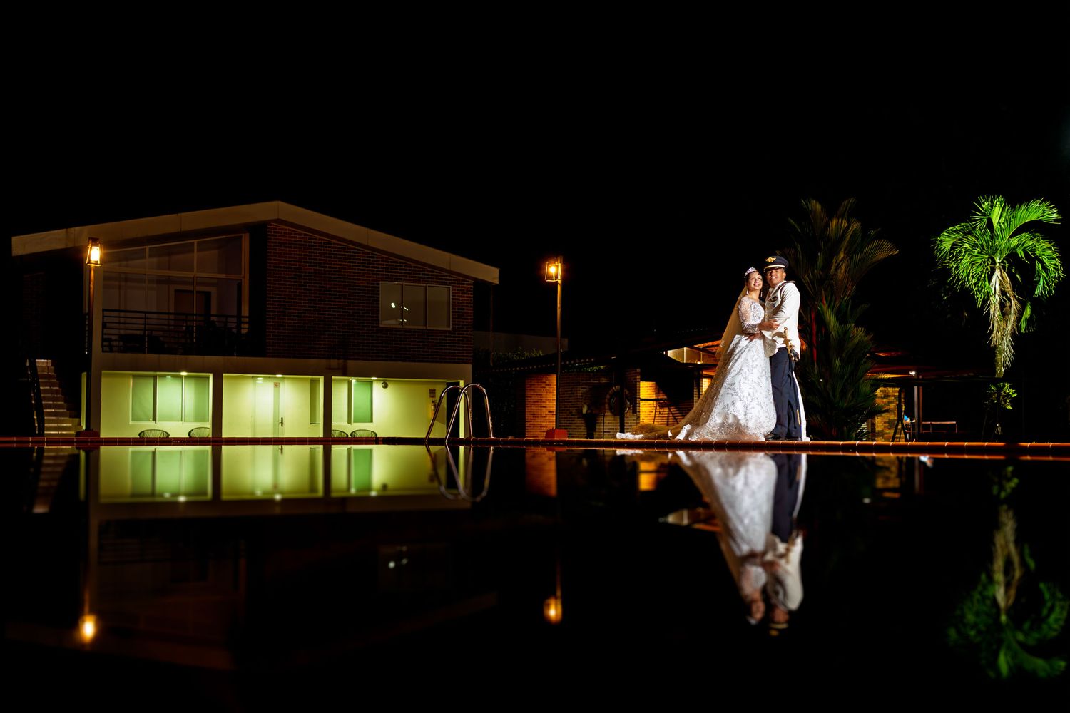 Retrato nocturno de los novios posando junto al reflejo de una piscina en Villavicencio