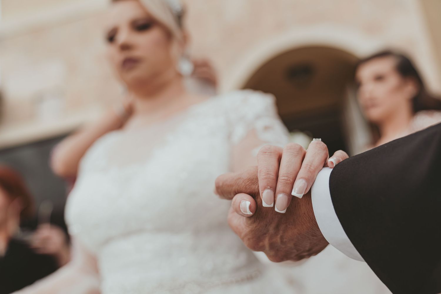 Detalle cercano manos: Novia (manicura francesa) sostiene mano de padre o familiar. Momento emotivo boda.