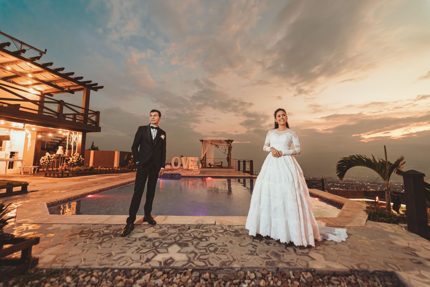Novios se abrazan junto a coche clásico en la puesta de sol. Foto romántica de boda con vehículo vintage.