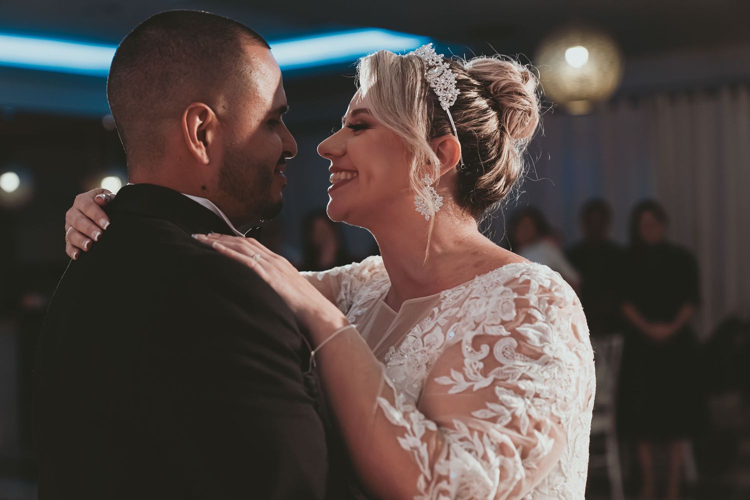 Primer plano: Novia sonríe feliz al novio mientras bailan juntos en recepción de boda; vestido encaje.