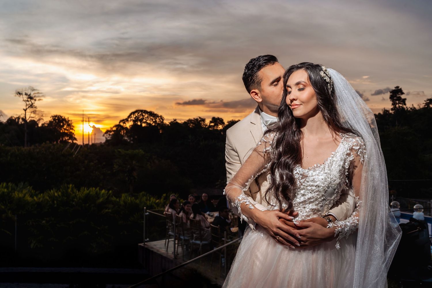 Novios se abrazan románticamente bajo un espectacular atardecer dorado sobre el paisaje. Foto de boda exterior.