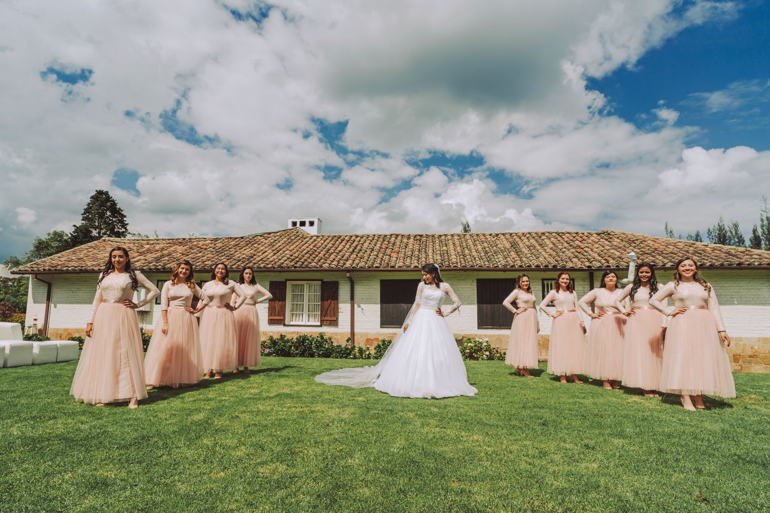 Novia posando con sus damas de honor en el jardín de una hacienda rústica.