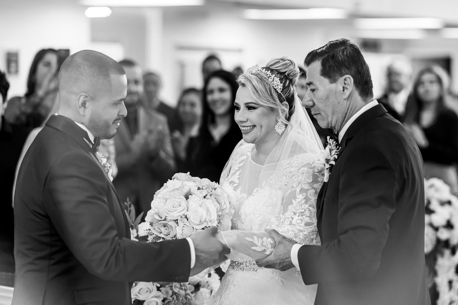 Foto B&W: Padre entrega mano de novia sonriente al novio en altar; momento emotivo ceremonia boda.